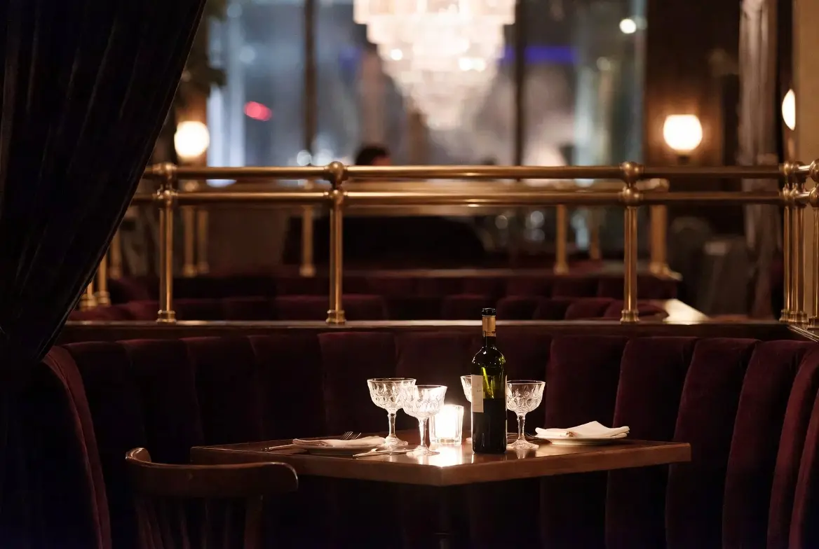 A just-vacated two-top table in an upscale Los Angeles restaurant — two empty coupe glasses, a partly-finished bottle of wine, candlelight.